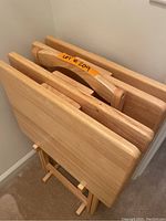 Wooden tray tables stacked together, showing smooth light wood with foldable stands