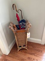 Wicker umbrella holder containing 3 umbrellas with wooden handles. The holder has a natural woven design.