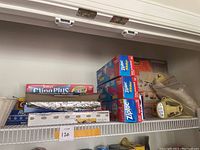 Shelf with boxes of Ziploc bags, Saran Plus cling wrap, rolls of aluminum foil, and tape dispenser.