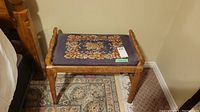 Front angled view of wooden needlepoint bench showing floral needlepoint seat and wood frame.