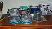 Image showing several clear glass bowls with various plastic lids in blue, green, and tan. Bowls are stacked and arranged on a shelf.