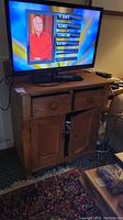 Wood cabinet shown with television on top, highlighting two drawers above and two doors below, natural wood finish, wood knobs.