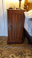 Front view of a wooden cabinet with vertical paneled door and brass knob, showing overall shape and finish.