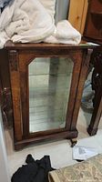 Full view of medium brown wood cabinet with glass door and mirror back, standing next to other furniture.