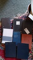 Top-down photo showing 8 journals of various sizes and colors arranged on a carpet with parts of a rug visible.