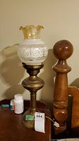 Full view of brass base table lamp with frosted glass shade showing floral decoration and amber ruffled top edge.