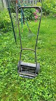 Photo of manual push lawn mower upright on grass showing rust on metal parts and plastic wheels.