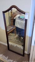 Full-length wood framed mirror standing against a wall. The mirror has a distinctive arch-shaped top and dark polished wooden frame.