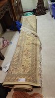 Rolled large decorative rug displayed indoors, showing detailed pattern and neutral color palette.