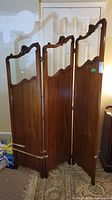 Full view of the three-panel wooden folding screen showing the carved wood frame, glass inserts, and hinged panels.