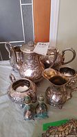 Front view capturing the entire silver plated tea set with coffee urn, cream and sugar bowl, small pitcher, and salt and pepper shakers on a table.