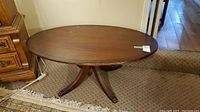 Front angled view of wooden oval coffee table showing oval tabletop, dark wood finish, brass ornamental feet on carved legs, scratches visible on tabletop surface.