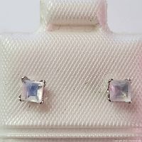 Front view of two square moonstone earrings in 10K white gold settings placed on display card.