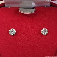 Pair of round cubic zirconia stud earrings in 14K yellow gold on red cushioned jewelry box background.