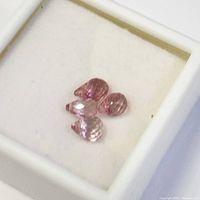 Photo showing four pear-shaped, faceted pink sapphire gemstones in a white jewelry box from a slightly angled view.