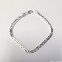 Silver bracelet laid out flat on a white surface showing full length and chain detail.