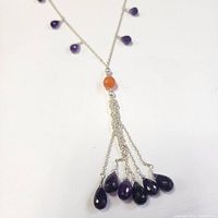 Close-up image of silver necklace with amethyst teardrop beads and a central carnelian bead with dangling amethyst bead tassels.