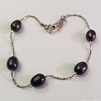 Close-up photo showing six irregularly shaped black freshwater pearls on a fine silver chain with lobster claw clasp.