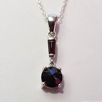Close-up image of the faceted round garnet stone pendant with a silver setting and part of the silver chain visible.