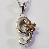 Close-up front view of silver rhodium plated pendant necklace with flower detail and diamond center.