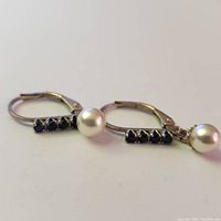 Close-up of the earrings showing 4 dark blue sapphire stones and hanging pearl on silver hoop.