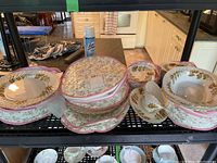 Photo showing stacked plates, cups, saucers, and serving items on metal shelving in kitchen