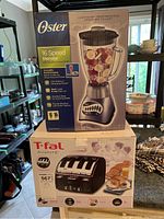 Front view of boxed Oster 16 speed blender and T-Fal four slice toaster stacked together.
