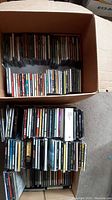 Two boxes filled with assorted music CDs stacked neatly, showing a large quantity of CDs.