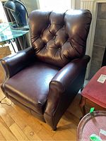 Front view of the brown leather reclining armchair showing tufted button detailing, cushioned armrests, and overall condition.