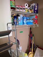 Shows shelf with cleaning sprays, wipes, Pine-Sol large bottle, rolls of paper towel, light bulbs packs.