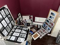 Wide view of large group of assorted photo frames on the floor against a maroon wall, showing variety of sizes and colors