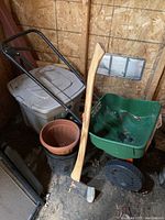 Broad view of garden tools and accessories including axe, pots, storage bin, and spreader