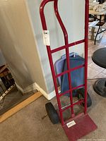 Full view of red hand truck showing the frame and flat loading plate against a carpeted floor.