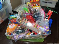Bin filled with various toys including TY figures in plastic bags, McDonald's collectible cars, and LEGO pieces with packaging visible