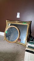 Three gold framed mirrors including one large ornate rectangular mirror and two round vintage mirrors. All placed on carpet against the wall.