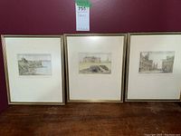 Photo showing three framed prints against a maroon wall and wooden surface, illustrating the lot contents.