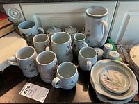 Full set of stoneware including mugs, steins, pitcher, salt and pepper shakers, and plates arranged together.