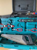 Set of assorted hand tools in open green plastic case showing handsaw, pliers, adjustable wrench, and level.