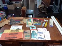 Overall view of the table with various model train pieces, instruction manuals, and rail memorabilia booklets spread out