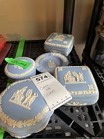 Five Wedgwood jasperware pieces displayed showing relief decorations, lids, and one chipped corner.