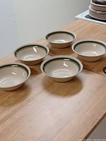 Five cream-colored ceramic bowls with green rims arranged on a wooden surface.
