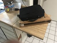 Photo showing a black laptop carrying case placed on top of a cardboard box on a kitchen counter, water bottles and various items in background.
