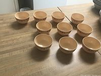 Ten small ceramic bowls arranged on a wooden surface, showing the exterior floral design and beige color.
