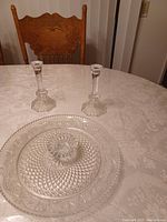 Photo of two clear crystal dishes, one larger and one smaller, with intricate cut designs placed on a lace tablecloth. In the background are two clear glass candlesticks with decorative bases.