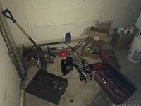Photo of multiple utilized car repair tools piled in corner including jacks, screwdrivers in toolbox, car oil with funnel, and various hand tools and hardware.