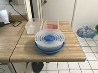 Photo showing seven nested round food storage containers with blue lids plus two separate square containers without lids on a countertop.