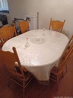 Oval dining table set up with six wooden chairs around it, covered with a transparent plastic sheet to protect the surface.