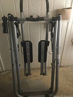 Photo of indoor walking exercise machine showing silver and black frame, foot pedals, adjustable handles, and built-in monitor