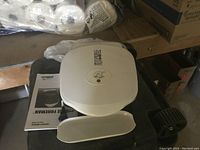 Photo showing the George Foreman Lean Mean Fat Reducing Grill in white with drip tray placed in front, boxed in storage area.