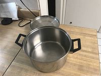 Photo showing large stainless steel cooking pot with black handles and matching stainless steel lid on a kitchen countertop.
